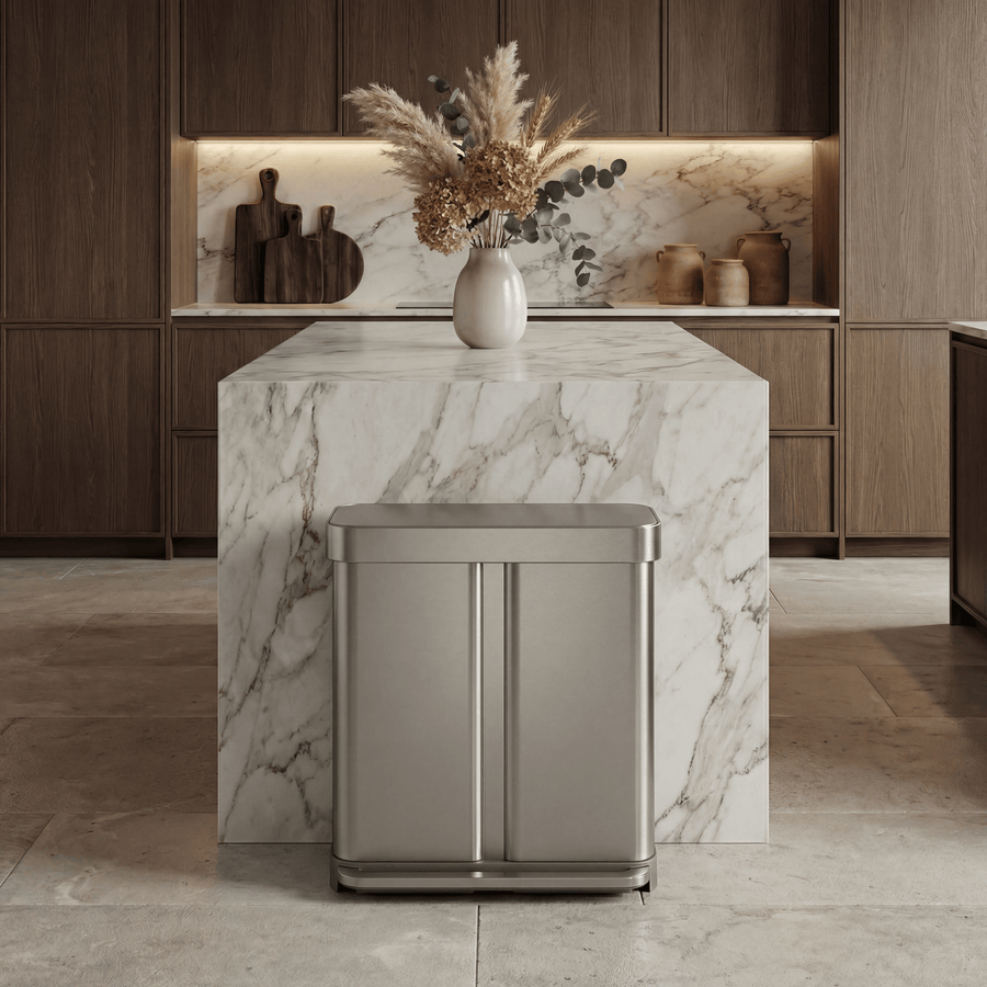 Simplehuman's 58L Step Recycler in brushed in a modern, luxury lived in home. The background features wooden cabinets, plants on a marble counter top and other counter appliances. 