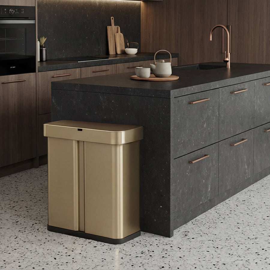 Simplehuman's Matte Gold Sensor Recycler along a black marble counter top with rose gold appliances and a few kitchen accessories.