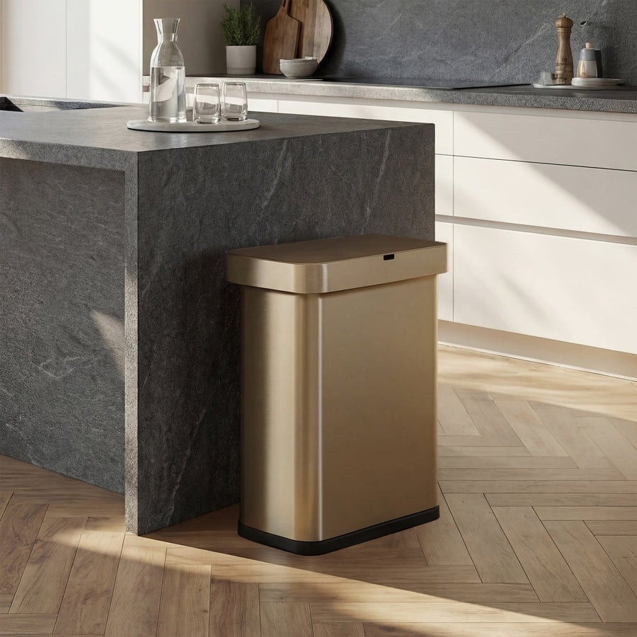 Simplehuman's Matte Gold Sensor Can in an elevated kitchen with marble and white appliances with the back side facing a marble counter.