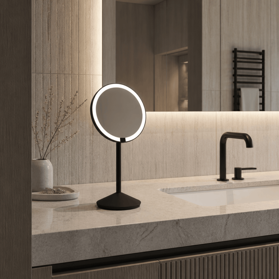 Simplehuman's Sensor Mirror Fold with 10x Magnification in Matte Black in a modern bathroom setting. 
